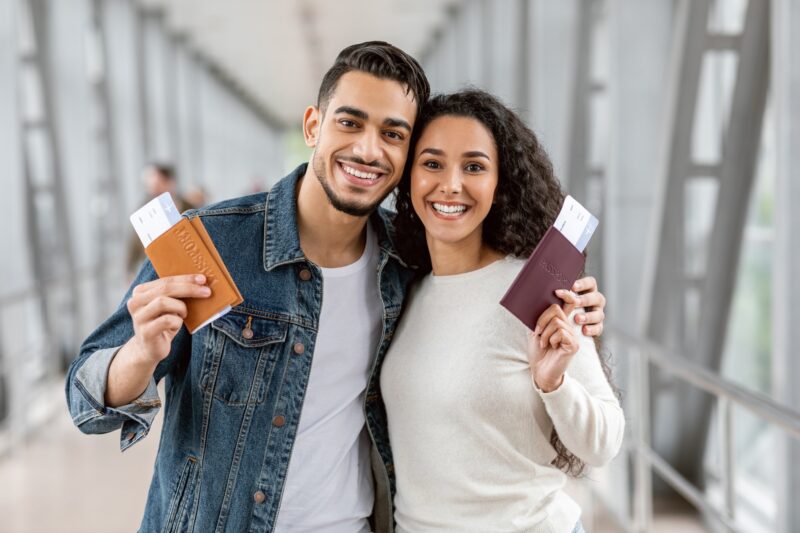 about 2 happy travellers young arab couple with passports and tickets posing at airport
